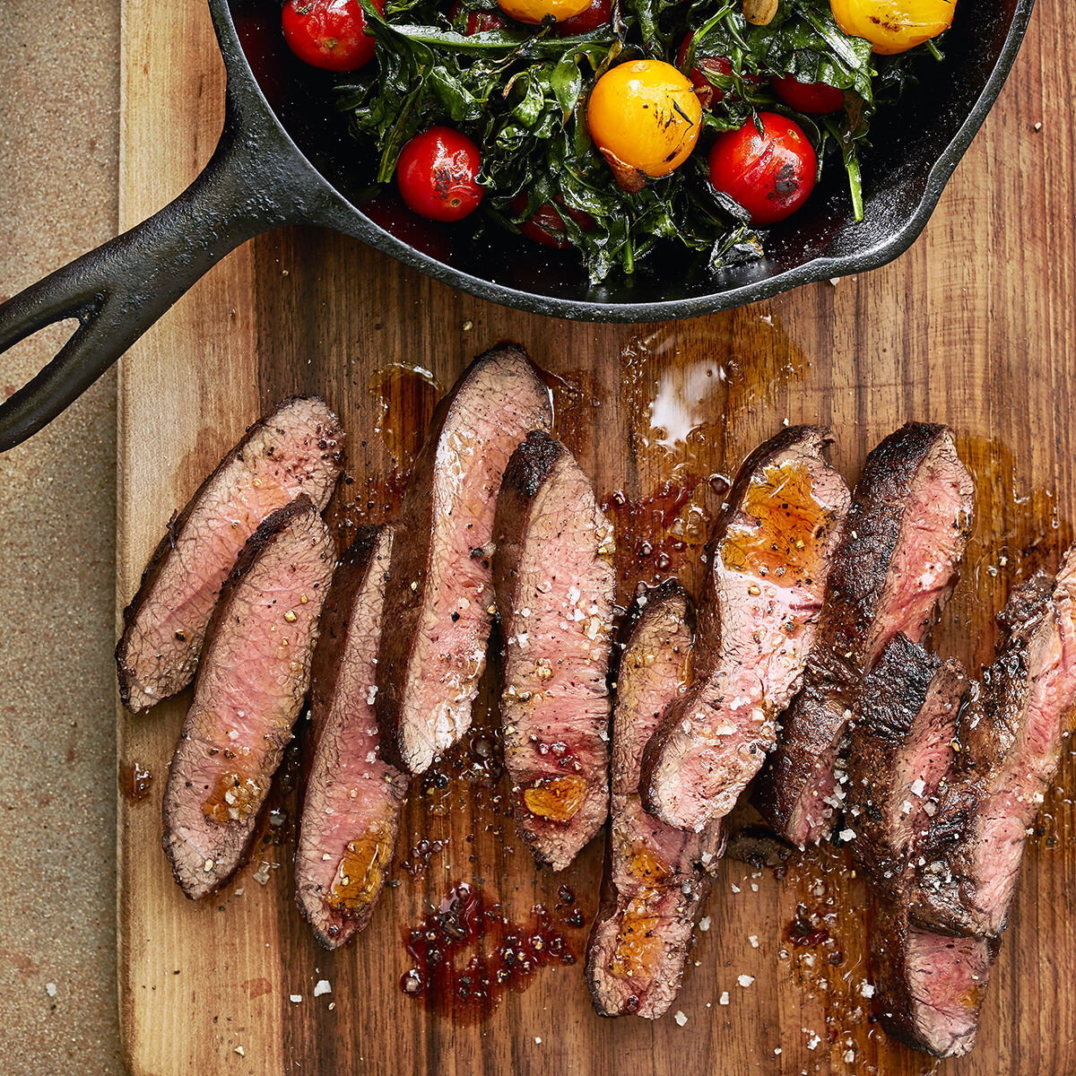 Seared Flat Iron Steak with Spigarello & Cherry Tomatoes on a skillet and a cutting board